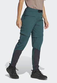Teal zippered pants with black accents, tapered fit, elastic cuffs, and adjustable waist. Made from lightweight, durable fabric.