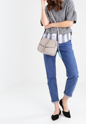 Szara torba crossbody z klapką, prostokątnego kształtu, o gładkiej skórzanej fakturze, z centralnym szwem i dekoracyjnym akcentem w postaci frędzla.