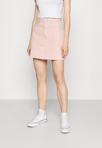 Gonna mini in denim rosa chiaro con orlo sfrangiato, presenta passanti per cintura e tasche frontali, abbinata a sneaker alte bianche.