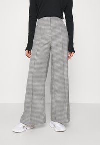 Högmidjade, vida byxor i svart och vitt houndstooth-mönster, tillverkade av ett texturerat tyg. Kombinerat med en svart långärmad topp.