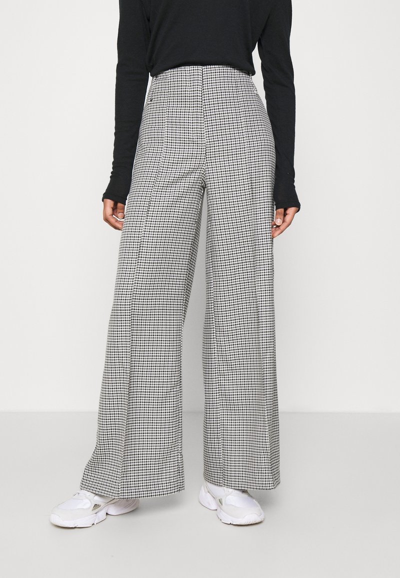 Högmidjade, vida byxor i svart och vitt houndstooth-mönster, tillverkade av ett texturerat tyg. Kombinerat med en svart långärmad topp.