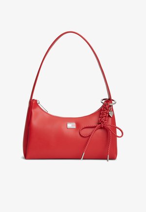 Bolso de cuero rojo para llevar al hombro con cremallera plateada, lazo trenzado decorativo rojo con colgante en forma de corazón y pequeña placa metálica rectangular con el logo.