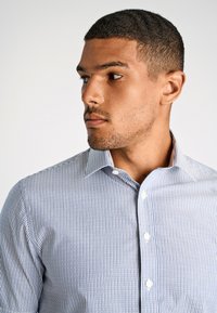 Camicia button-up con un motivo a righe sottili blu chiaro e bianche, con colletto, caratterizzata da una texture di cotone morbido e bottoni bianchi.