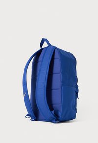 Blue backpack with a smooth fabric texture, padded back, adjustable straps, and a small side pocket. Features a yellow logo accent.