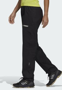 Pantaloni neri impermeabili con vita regolabile, dotati di logo TERREX e dettagli riflettenti. Tessuto dalla texture liscia, progettati per attività all'aperto.