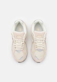 Beige sneakers med nät- och mockadetaljer. Har en rund tå, snörning, vadderad krage och en kontrastlogotyp på sidan.