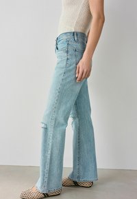 Lichtblauwe spijkerbroek met flair heeft een hoge taille, verstoorde kniedetails en een schone afwerking. Gepaard met patroonballerina's en een gebreide top.
