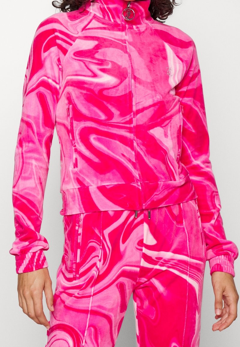 Velour-träningsjacka i livlig rosa med vitt marmoreringmönster, hög krage, blixtlås och sidofickor. Mjuk, texturerad yta.