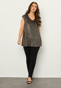 Top de lentejuelas brillantes con escote en V y mangas cortas, que presenta un diseño plisado en tonos de bronce, combinado con pantalones ajustados negros.