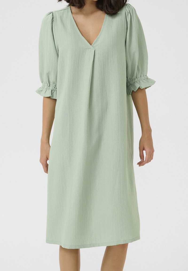 Robe vert clair avec un col en V, des manches bouffantes et des poignets froncés. Fabriquée en tissu texturé, longueur genou avec une coupe ample.