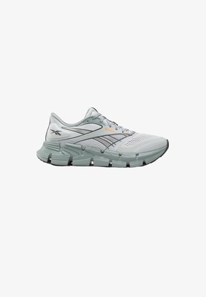 Lichtgrijze Reebok hardloopschoen met een bovenwerk van mesh, een dikke gesegmenteerde zool, zwarte accenten en een oranje logo aan de zijkant, gezien vanaf de buitenkant.