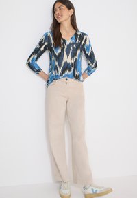 Haut à manches longues bleu et crème à motifs, associé à un pantalon en velours côtelé beige et des baskets blanches avec des accents bleus. Texture lisse, coupe décontractée.