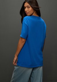 Blue cotton t-shirt with short sleeves and a relaxed fit. The back features a round neckline and visible stitching details.