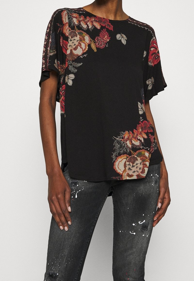 Svart kortärmad topp med blommönster i rött, gult och blått. Har en avslappnad passform och delikat broderi längs axlarna.