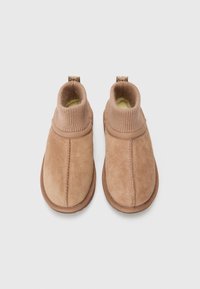 Bottes chelsea en cuir suédé marron avec une bordure en tricot côtelé, bout arrondi et semelle en caoutchouc texturé. Présente des coutures le long des côtés.