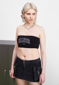 Juodas frotinio audinio be petnešų švarkelis su 'ELLESSE' logotipu; juoda džinsinė mini sijonas su priekiniais užtrauktukais ir šoninėmis kišenėmis; tekstūruotas audinys.