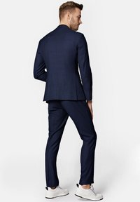 Granatowy, w kratkę garnitur z usztywnioną marynarką i dopasowanymi spodniami, wykonany z materiału miksowanego. Połączony z białymi sneakersami dla nowoczesnego wyglądu.