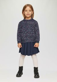 Dunkelblauer Strickpullover mit rosa Akzenten, plissierter marineblauer Rock, weiße Strumpfhose und schwarze ankle boots. Einfaches, geschichtetes Outfit für Kinder.