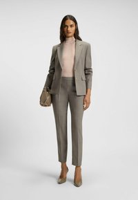 Grau karierter Blazer und passende maßgeschneiderte Hose über einem hellrosa Rollkragenpullover, kombiniert mit einer beigen Handtasche und spitzen Absatzschuhen.
