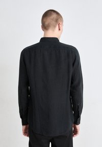 Svart långärmad skjorta med knappar och krage, rak skärning och något böjd fåll. Tyget verkar lätt och har en slät textur.