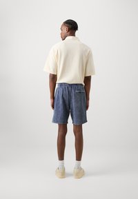Polo à manches courtes jaune clair avec un motif texturé, assorti à un short en denim bleu avec une taille élastique et une poche à l'arrière.
