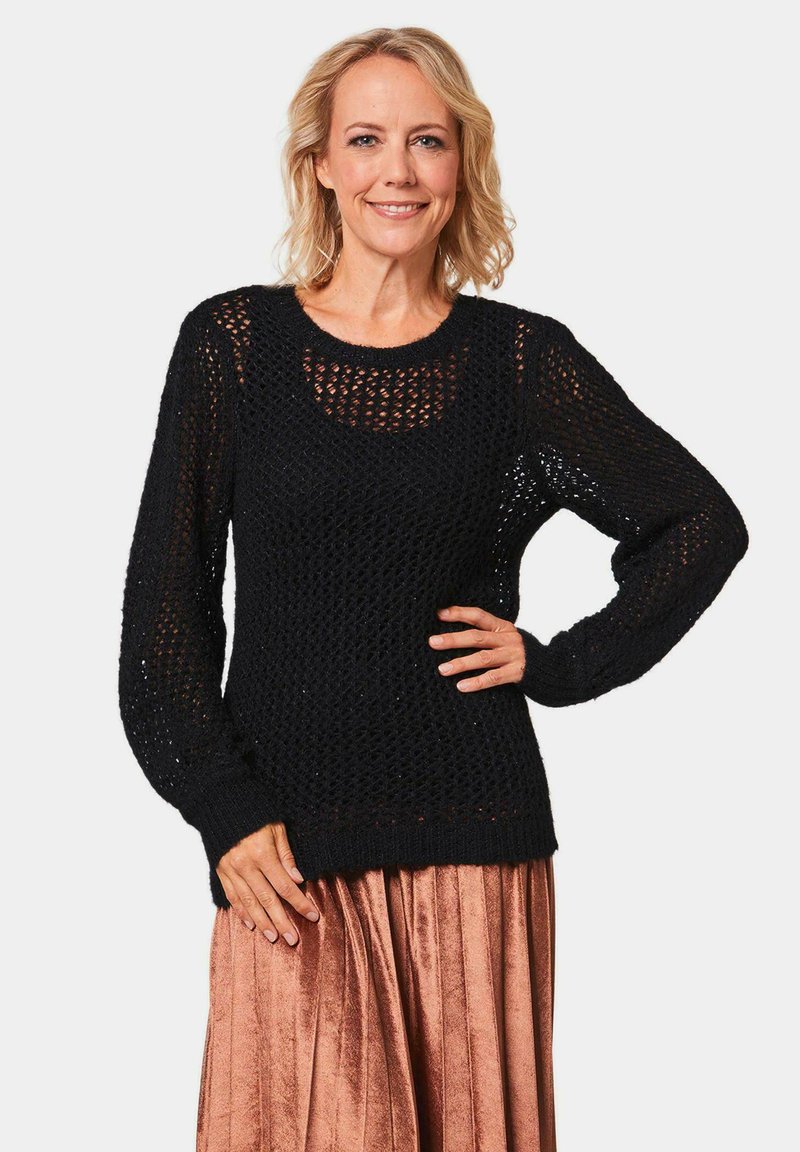 Zwarte gebreide trui met een open weefsel, ronde halslijn en lange mouwen, gecombineerd met een geplooide metallic rok.
