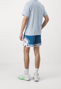 Vaaleansininen puuvillapaita pyöreällä kaula-aukolla, yhdistettynä sinisiin shortseihin, joissa on valkoinen yksityiskohta ja Jordan-logo. Valkoiset ja vihreät lenkkarit.