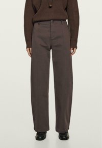 Brun ribbet sweater parret med høj talje, brede grå bukser med foran syninger, en knaplukning og en glat overflade.