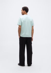 Μπλουζάκι κοντομάνικο σε μέντα πράσινο, άνετη εφαρμογή, κατασκευασμένο από βαμβάκι, συνδυασμένο με μαύρο παντελόνι cargo με πλαϊνές τσέπες και ίσια γραμμή.