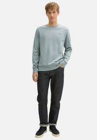 Hellblaue Langarm-Sweatshirt aus weichem Stoff, kombiniert mit dunklen Jeans. Einfaches Rundhals-Design mit einem dezenten Logodetail.