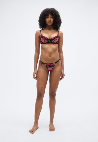 Conjunto de lencería con tela rosa transparente y superposición de encaje floral negro, tirantes ajustables y lazos decorativos en la parte inferior tipo bikini.