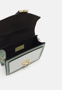 Borsa strutturata verde e bianca con interno nero, dotata di una chiusura dorata e di un'etichetta. Texture liscia, forma rettangolare, doppio anello in metallo.