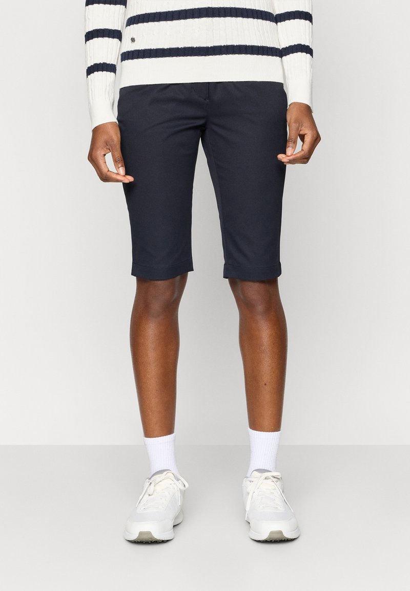 Marineblå shorts med skreddersydd passform, oppbrettede kanter og sidelommer, sammen med hvite sneakers og en ribbestrikket genser med marineblå striper.