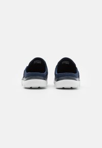 Navy slip-on shoes with a textured mesh upper, white midsole, and rounded sole. Features minimal branding and a smooth back opening.
