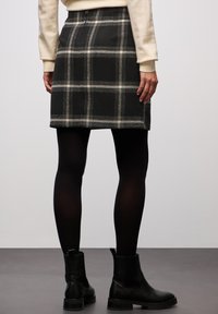 Zwart-witte geruite rok van textuurstof, met een aansluitend ontwerp en een rechte snit, gecombineerd met zwarte enkellaarsjes.