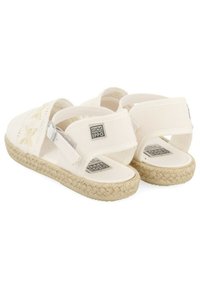 Sandales en tissu blanc avec un design tissé, des lanières ajustables et une semelle en corde de jute. Étiquette de marque visible au niveau du talon.
