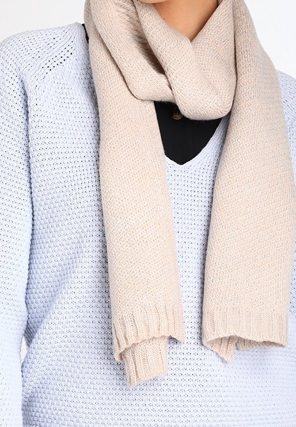 Écharpe beige en tricot enveloppée autour du cou, portée sur un pull bleu clair texturé avec une chemise noire en dessous.