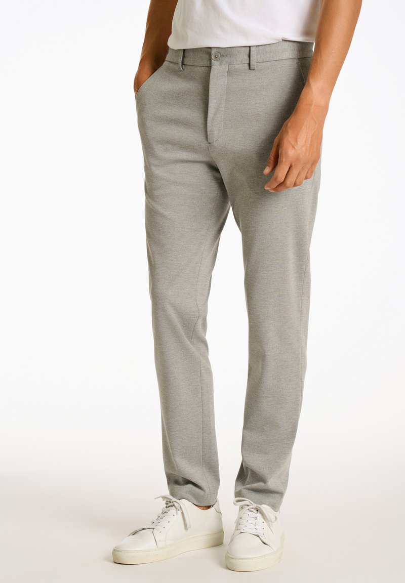 Grijze op maat gemaakte broek met een gladde textuur, voorzien van een platte voorkant, zijzakken en een slim fit. Gecombineerd met witte sneakers.