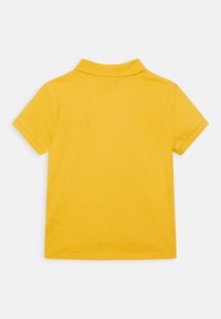 Keltainen, lyhythihainen polo-paita, jossa on pehmeä tekstuuri, ribbireunus ja puhdas muotoilu. Takana ei ole näkyvissä logoja tai kuvioita.