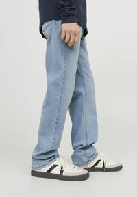 Jeans de mezclilla azul claro con un corte relajado, que presentan un diseño clásico de cinco bolsillo y una sutil textura desgastada, combinados con zapatillas blancas.
