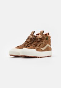 Brune semskede høyde sneakers med hvit gummisåle, rund tå og brune snører. Har side stripe og hælflik detaljer.
