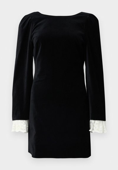 Crna baršunasta haljina dugih rukava, s bijelim čipkastim detaljima na manžetama i kvadratnim izrezom. Glatka tekstura, prilagođen oblik.