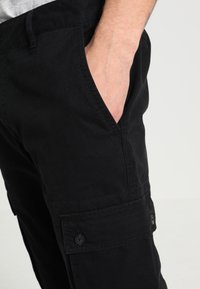 Pantaloni cargo neri realizzati in cotone, dotati di tasche laterali, una texture liscia e dettagli con bottoni per una chiusura sicura.