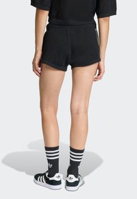 Čierne pletené šortky s textúrovanou tkaninou, priliehavým pásom a kontrastnými rebrovanými lemami. Kombinované s čierno-bielymi pruhovanými ponožkami a teniskami.