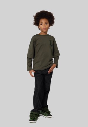 Khaki lange mouw t-shirt met een klein donkergroen logo, gecombineerd met zwarte jeans en opvallende groene en zwarte gestructureerde sneakers.