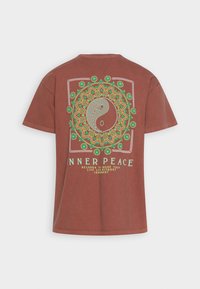 Brun bomull T-shirt med ett mandala-mönster i grönt och gult, tillsammans med en yin-yang-symbol och texten "INRE FRID" nedan.