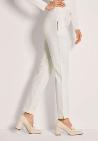 Witte slim-fit jeans met een middelhoge taille, zakken en een klein ritsdetail. Gepaard met beige hoge hakken. Glad van textuur.