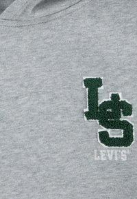 Sudadera de algodón gris con un logo bordado en verde oscuro que contiene "LS" y un signo de dólar, junto con "LEVI'S" en blanco debajo.