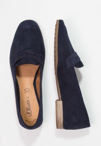 Granatowe zamszowe loafersy z płaską, brązową gumową podeszwą. Posiadają ozdobny pasek oraz wycięcia. Wnętrze jest z beżowego zamszu.