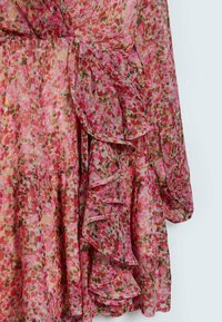 Robe florale rose transparente à manches longues avec des volants superposés le long du devant et de l'ourlet.